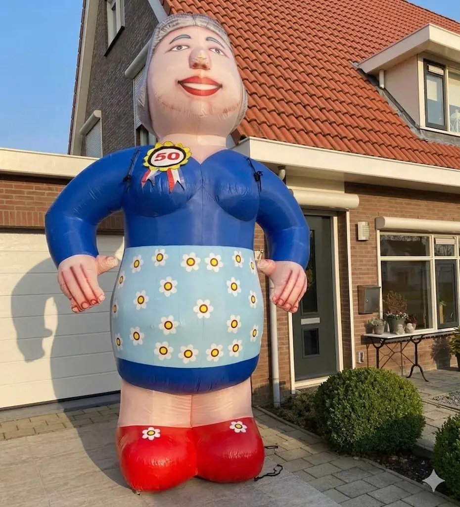 Opblaasfiguur Sarah met blauwe jurk, bloemenschort en rode schoenen in een voortuin